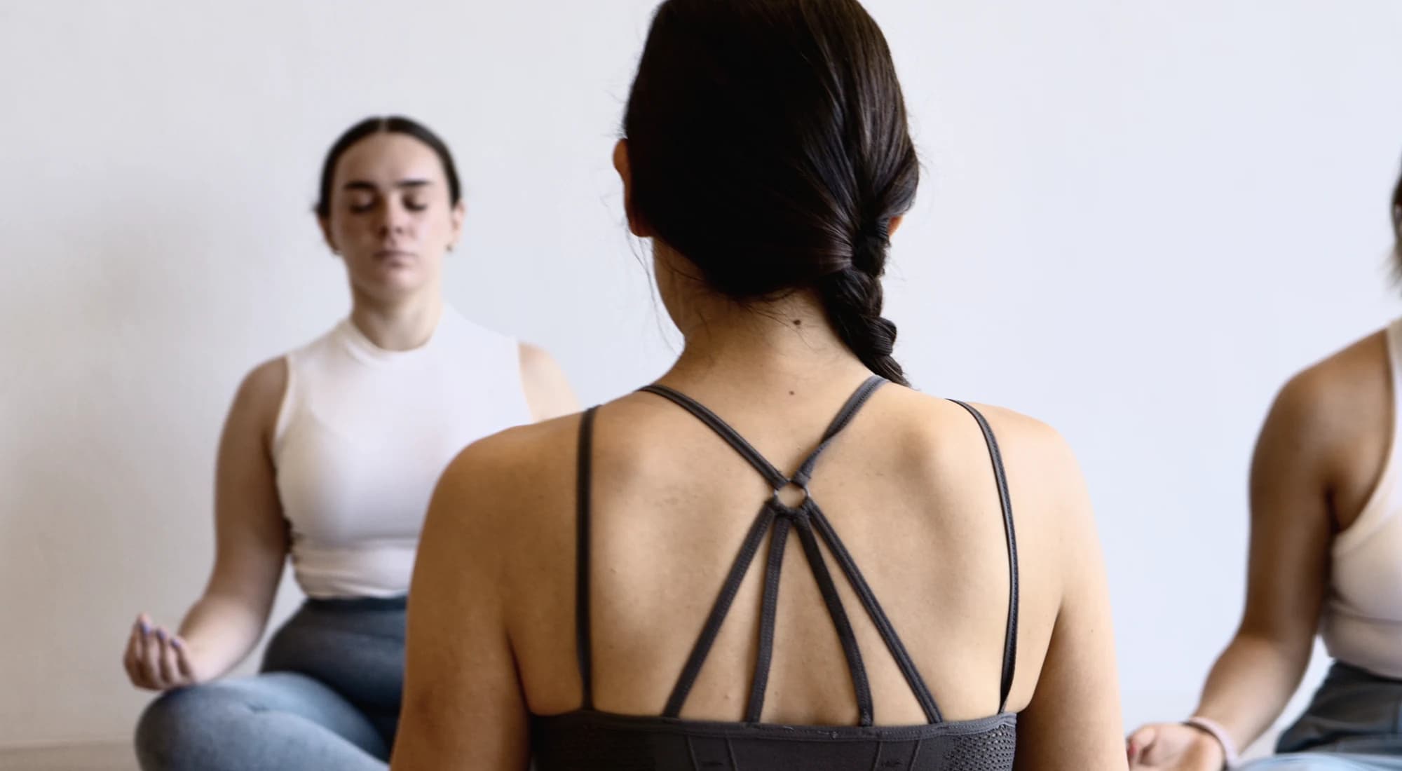 Tres personas sentadas en meditación en el salón de Vitala, contra la pared clara